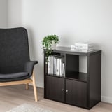 Moderne stuescene med KALLAX sort hylde, stilfuld sort stol, bøger og plante, der fremhæver kontraster i størrelse og indretning.