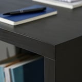 Sort skrivebord med glat overflade, der viser kvalitetshåndværk. I nærheden hviler en kuglepen på en blå notesbog, der understreger et pænt og organiseret arbejdsområde.