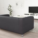 Moderne stue med sort KLIPPAN sofa, hvidt sofabord, tv på stativ, plante og abstrakt vægkunst.