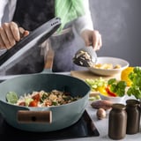 Krydderet i KLIPPFISK pande. Træhåndtag, non-stick belægning, omgivet af friske råvarer.