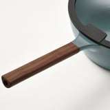 Nærbillede af et moderne sauterhåndtag. Mørkebrunt træ, slankt design, fastgjort til glat, lyseblå pande.