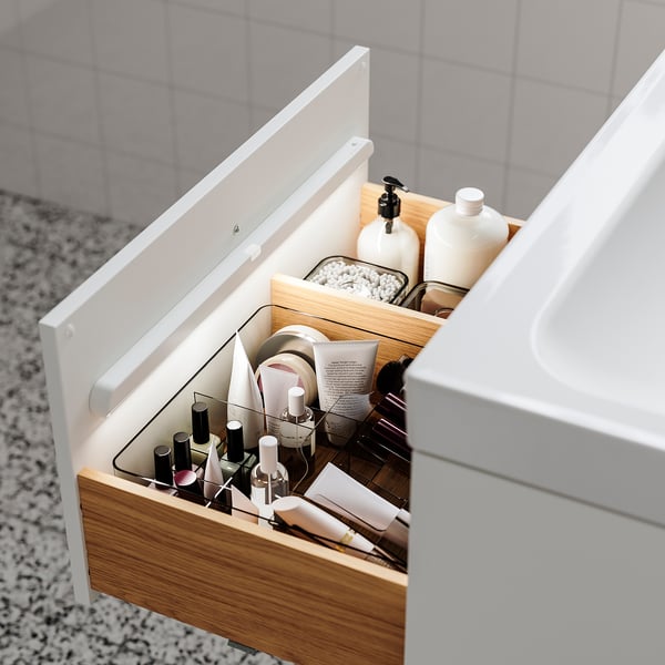 Åben træskuffe med organiserede toiletartikler, herunder neglelakker og flasker. Blødt lys oplyser automatisk indholdet.