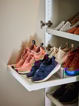 En skabshylde med hvide skuffer med farverige sneakers i lyserøde og blå nuancer med en filtindsats.