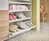 En hvid skohylde med tre hylder, der opbevarer sneakers i forskellige farver. Lysegrøn væg.