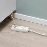 Hvid multi-socket enhed på trægulv, der udvider strømkapaciteten fra nærliggende stikkontakt.