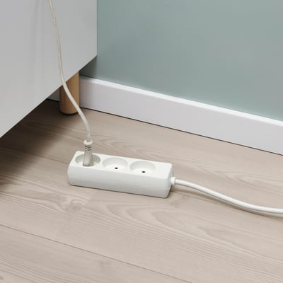 Hvid multi-socket enhed på trægulv, der udvider strømkapaciteten fra nærliggende stikkontakt.