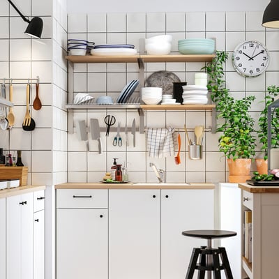 Moderne køkken med træborde, hvide skabe, magnetisk knivstativ, planter, skammel, ur.
