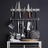 Væghængt køkkenopbevaring med knive, redskaber og holder på mørk baggrund.
