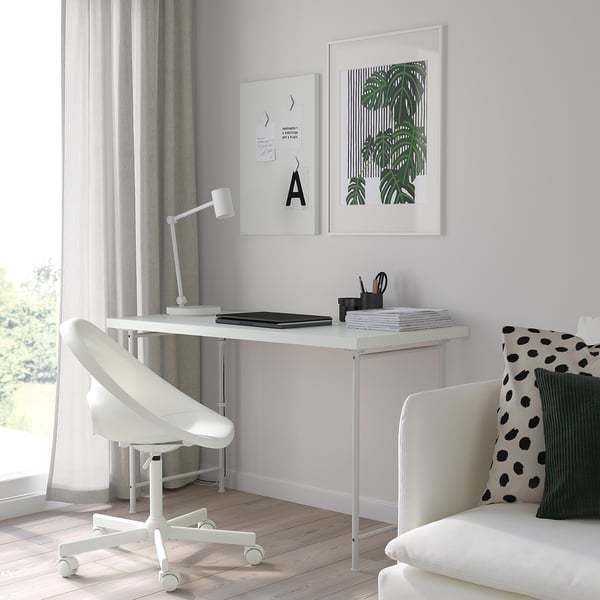 Minimalistisk hjemmekontor: LAGKAPTEN skrivebord, stol, lampe, bærbar computer, notesblok, penneholder, kunst, hvid sofa med hynder.