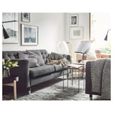 Moderne stue med grå stofsofa, mønstrede puder, metallisk sidebord og vægkunst.