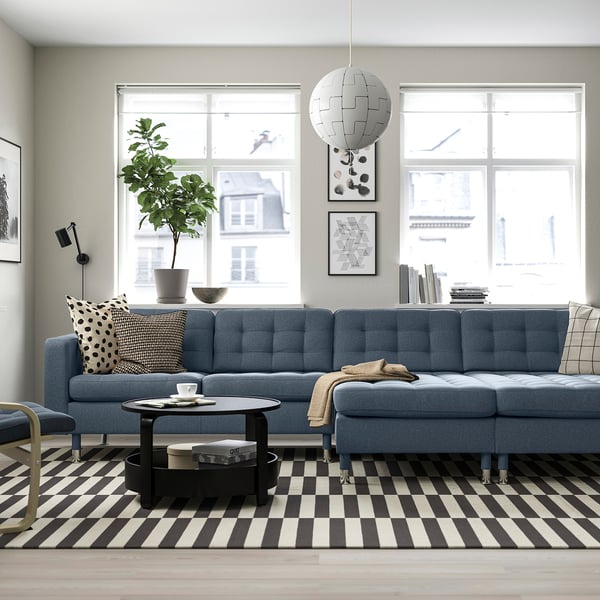Moderne stue med blå sofa, ternet tæppe, sofabord, puder, plante og hvid pendel.