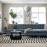 Moderne stue med blå sofa, ternet tæppe, sofabord, puder, plante og hvid pendel.