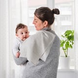 En kvinde holder en baby ved hjælp af en grå musselinklud til beskyttelse. Kluden er slidstærk og skånsom mod huden, perfekt til skift eller eftermadning.