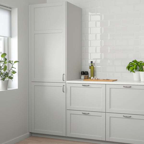 Moderne lysegråt LERHYTTAN køkken med skabe i massivt træ, planter og bagplade. Høje enheder tårner sig op over disken med flaske og redskaber.