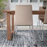 Moderne spisebordsopsætning med beige LILLÅNÄS-stole omkring et træbord på et mønstret tæppe, med ergonomiske sæder og krom slædebunde.