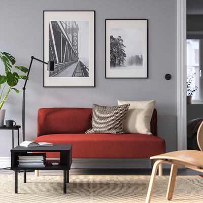 Moderne stue med rød sofa, sort sofabord, tæppe, fotos og træstol ved dør.