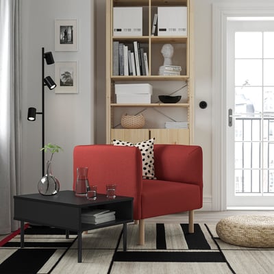 Moderne stue med rød lillem sofa, sort sofabord, sort og hvidt tæppe, træreol og sort gulvlampe.