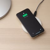 En smartphone oplades trådløst på en flad pude, der viser 67 % opladning med en grøn indikator.