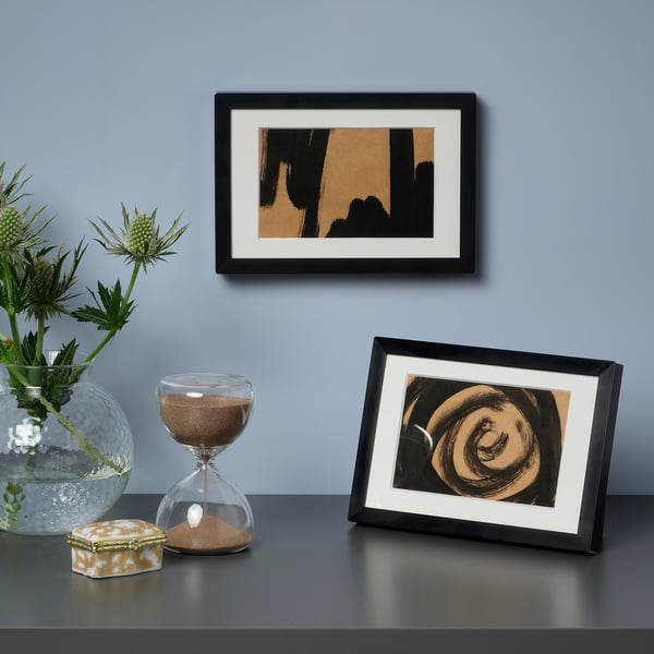 Kunsttryk og dekoration på bordet: abstrakt kunstværk, timeglas, vase med planter.