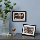 Indrammet foto og abstrakt kunst mod væg. Glasvase med planter og timeglas.