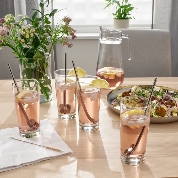 Fire glas med lyserøde drinks og citronskiver på et bord sammen med en kande og salat.
