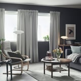 Moderne stue med grå MAJGULL gardiner, hyggestol, sofabord, blomster, drikkevarer, gulvlampe, skrivebord og kunst.