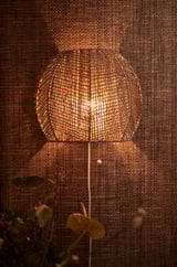 En oplyst, håndflettet lampe med varmt, gyldent lys. Lavet af naturlig star, unikt design med træksnor.