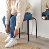 Person sidder på sort MARIUS skammel, binder hvid sneaker, afslappet indstilling.