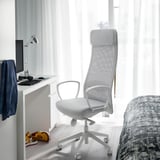 Ergonomisk MARKUS stol ved skrivebordet med skærm, støttende, hjemmekontor, tæt på vindue og seng.