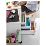 En person laver med farvet papir og origami ved hjælp af et hvidt MICKE-skrivebord med åbne skuffer fyldt med forsyninger.