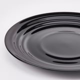 Rund, sort plade med et blankt, bølget design på en hvid overflade, der reflekterer lyset, viser håndværk af høj kvalitet og slank finish.