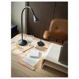 Veloplyst hjemmekontor med NÄVLINGE sort moderne lampe på træbord, brun stol, bøger og tekniske enheder.