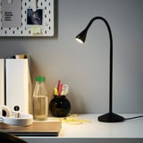 Moderne minimalistisk skrivebordsopsætning med sort NÄVLINGE lampe. Slankt, fleksibelt design. Skrivebordet rummer også hovedtelefoner, vandflaske og kontorartikler.