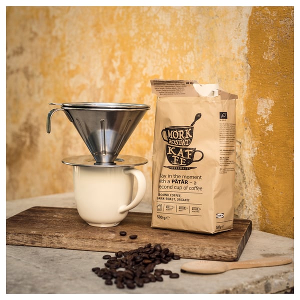 Hæld kaffemaskine over med kaffebønner på krus mod gul væg.