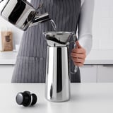 Hæld vand i en slank, moderne kaffemaskine med genanvendeligt filter på bordpladen.