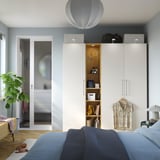 Moderne soveværelse med hvid PAX garderobe, blå seng og spejlreflekterende plante.