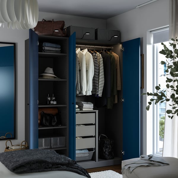 Blå garderobe med pænt tøj, håndklæder og tilbehør. I nærheden af et vindue og en plante.