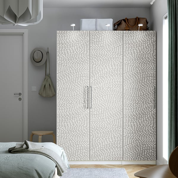 Minimalistisk værelse med højt gråt PAX garderobeskab, to hvide kasser, brun taske, træskammel med hat og delvis udsigt til sengen.