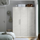 Minimalistisk værelse med højt gråt PAX garderobeskab, to hvide kasser, brun taske, træskammel med hat og delvis udsigt til sengen.