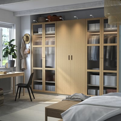 Moderne soveværelse med ikea PAX garderobeskab, blanding af massive og glasdøre, nær vindue med skrivebord og stol.