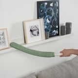 En hånd, der holder en grøn PEPPRIG mikrofiber-støvsuger og strækker den vandret over en hvid hylde med vægdekoration.