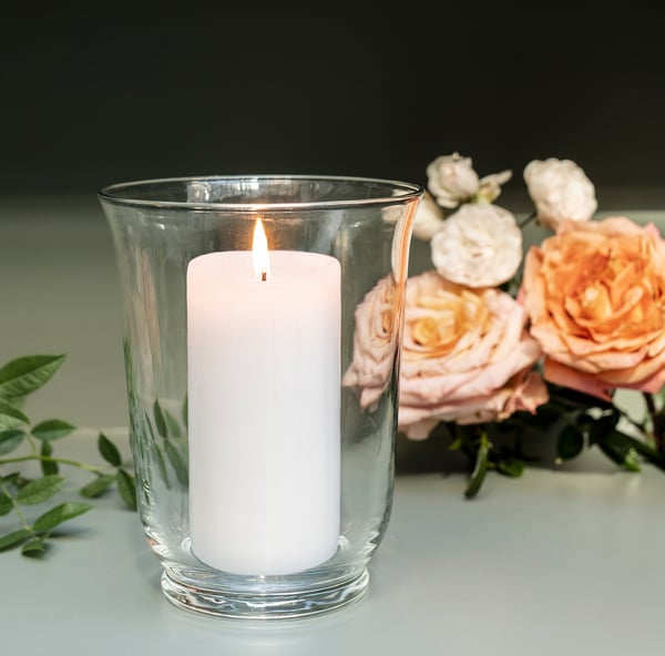 Lysestage i klart glas med hvidt stearinlys og lyserøde roser.