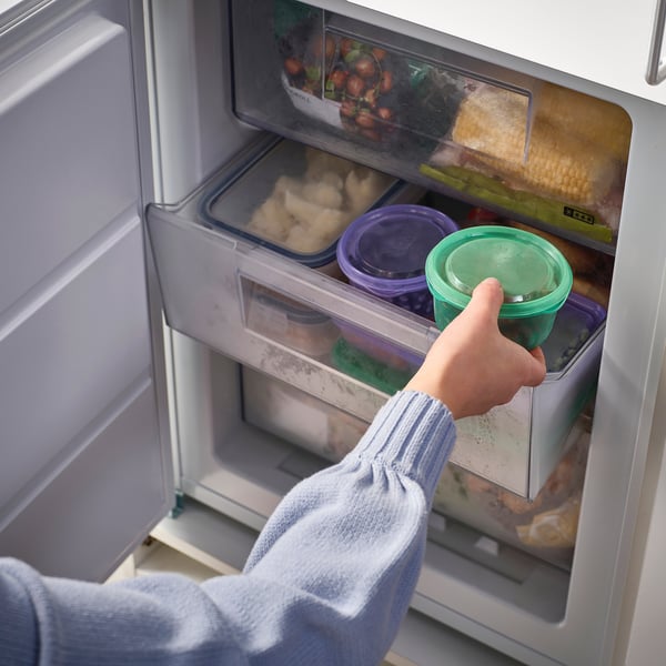 Person, der tager en grøn beholder fra køleskabet, opbevarer rester eller snacks, ideel til skole- eller arbejdsfrokoster.