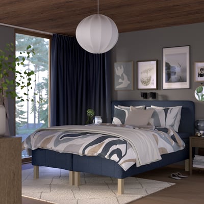 Moderne soveværelse med RÅHOLMAR seng, blågrå, træ, firkantet, sengetøj med geometrisk tryk, hængende lampe, mørke gardiner, kunst, planter, hyggeligt.