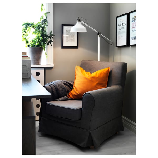 Hyggelig læsekrog med grå RANARP lampe, orange pude og grå lænestol ved vindue med plante.
