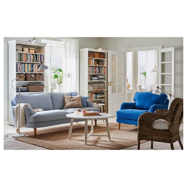 Lys stue med blå sofa, kurvestol og bogreoler med bøger og lamper.