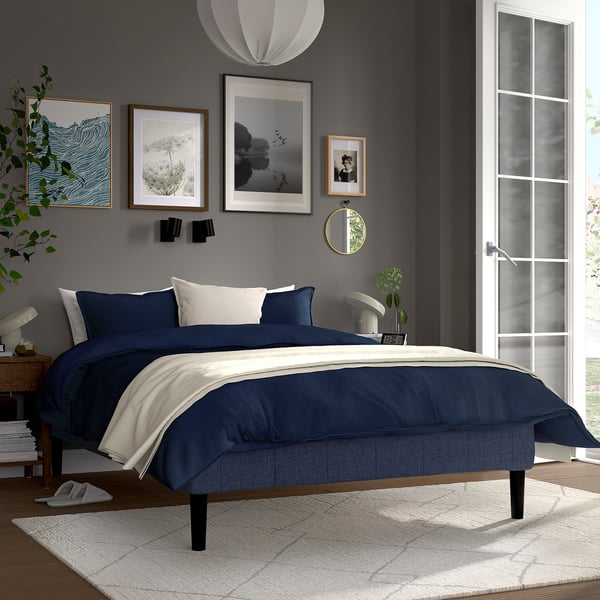 Et moderne soveværelse med en RENFJÄLLET seng med blå og hvid indretning, minimalistisk kunst, et blødt tæppe og en fredfyldt atmosfære.