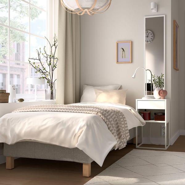 Minimalistisk soveværelse med RENFJÄLLET seng, puder, dyne, natbord, rød boks, plante, lampe.