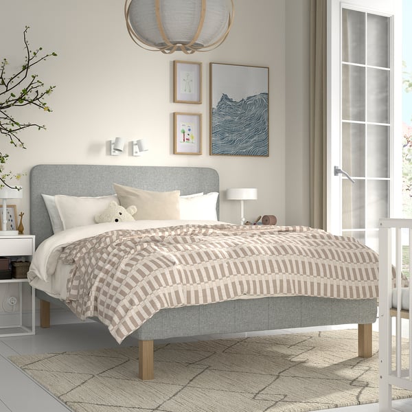 Moderne grå seng med stribet beige dyne, hvide puder. Stor kunst, bjørnelegetøj, træben. Størrelse: konge.