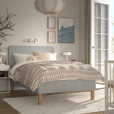 Hyggeligt soveværelse med RENFJÄLLET seng, grå sengegavl, beige/hvidt sengetæppe, bamsepude, blød lampe, moderne kunstværker, stort hvidt tæppe.